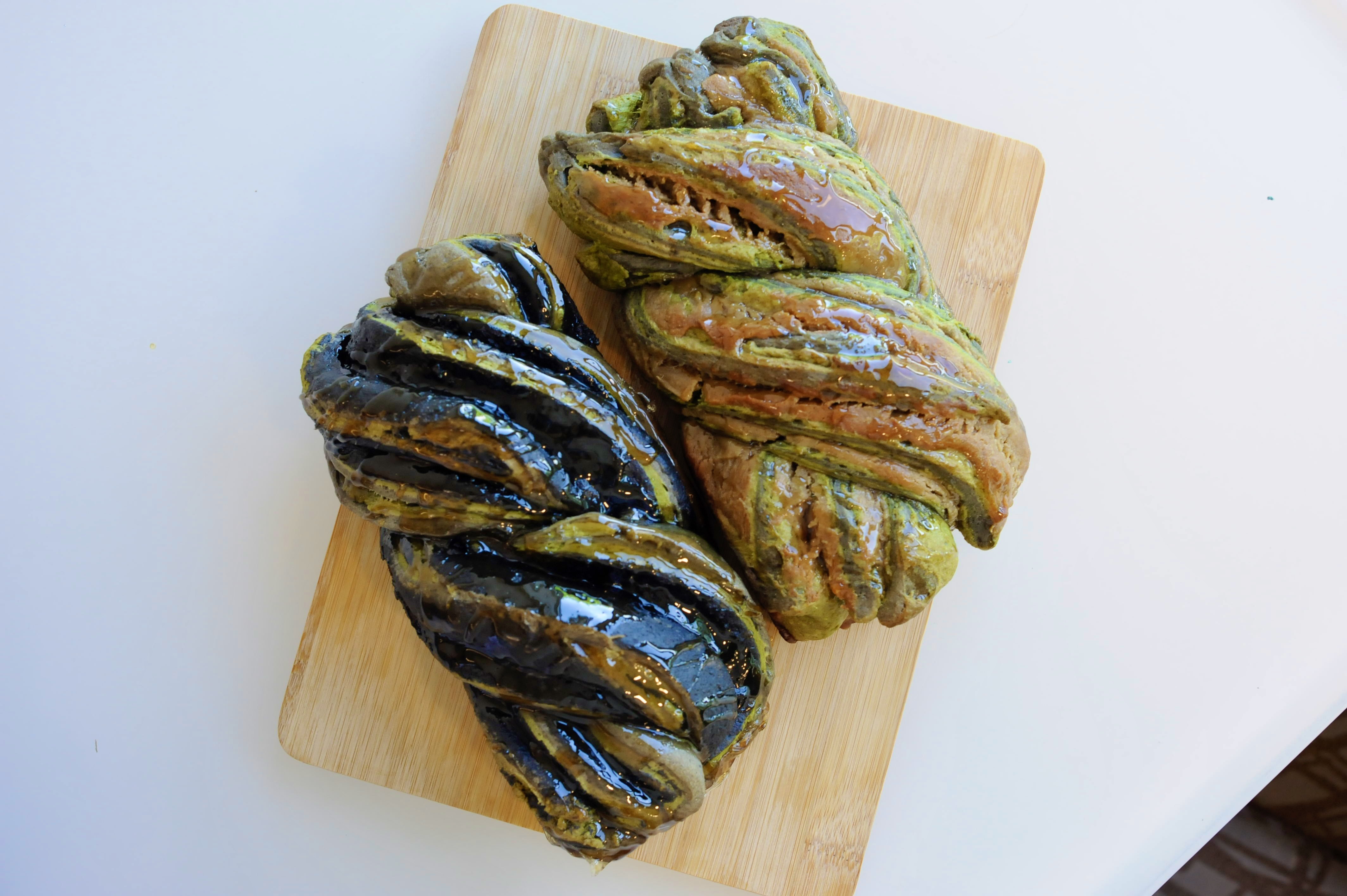 an overhead shot of two loaves of braided challah bread with black and green swirls.